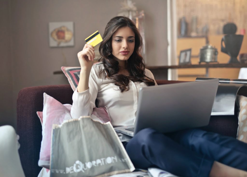 Woman on couch with laptop, credit card, and shopping bag